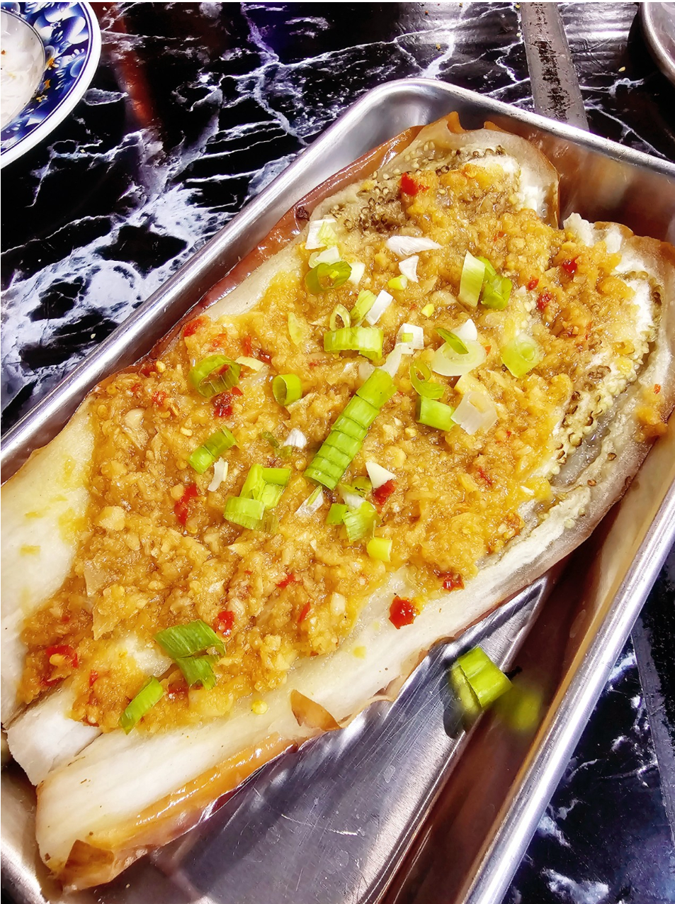 Grilled fish topped with minced garlic, scallions, and chili in a metal tray