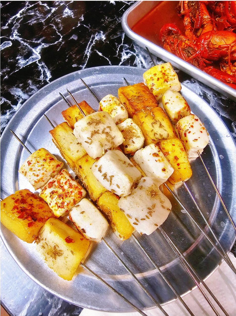 Grilled skewers with tofu, potato slices, and spices on a metal plate