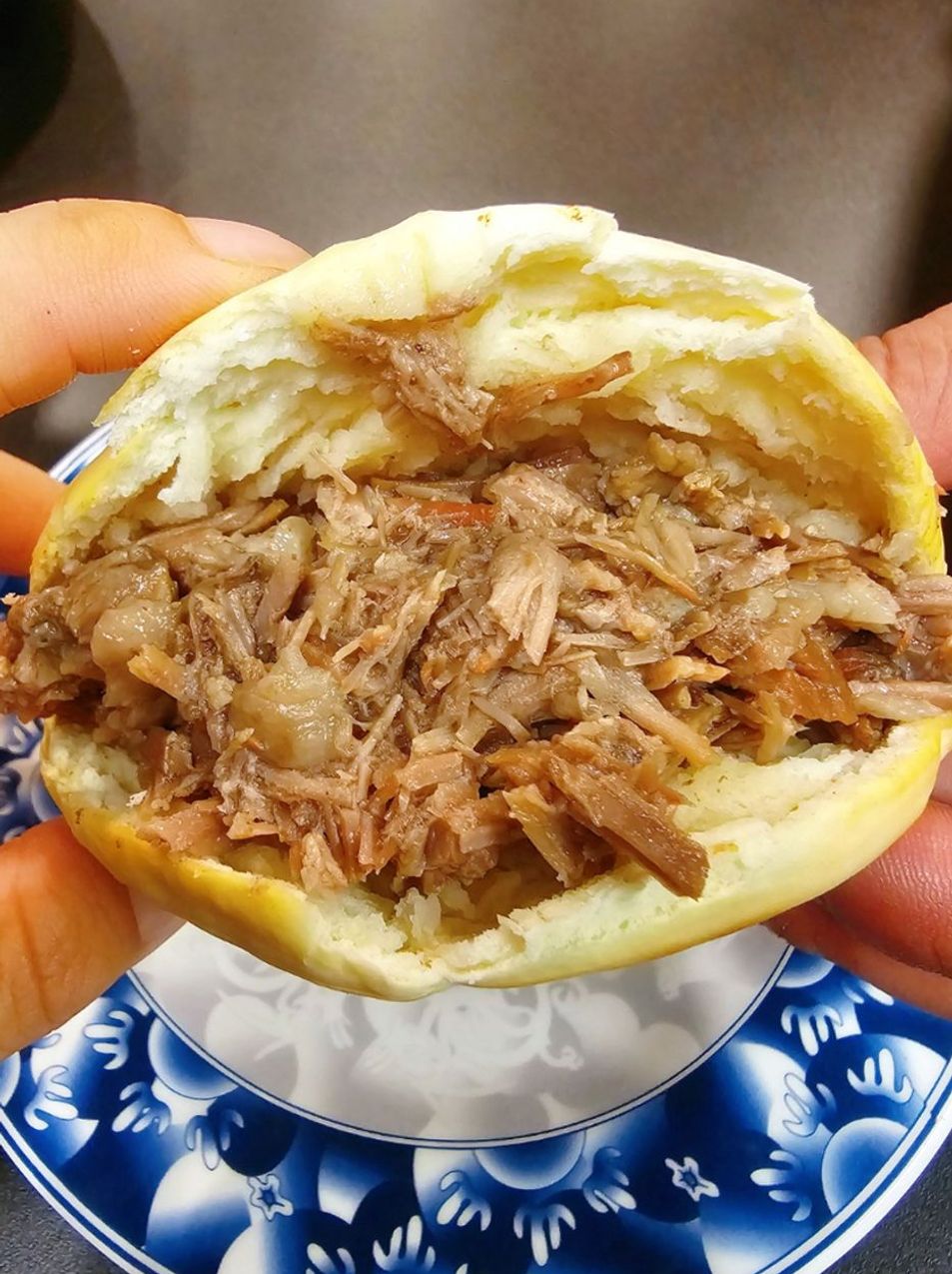 Hand holding a split bun filled with shredded braised meat