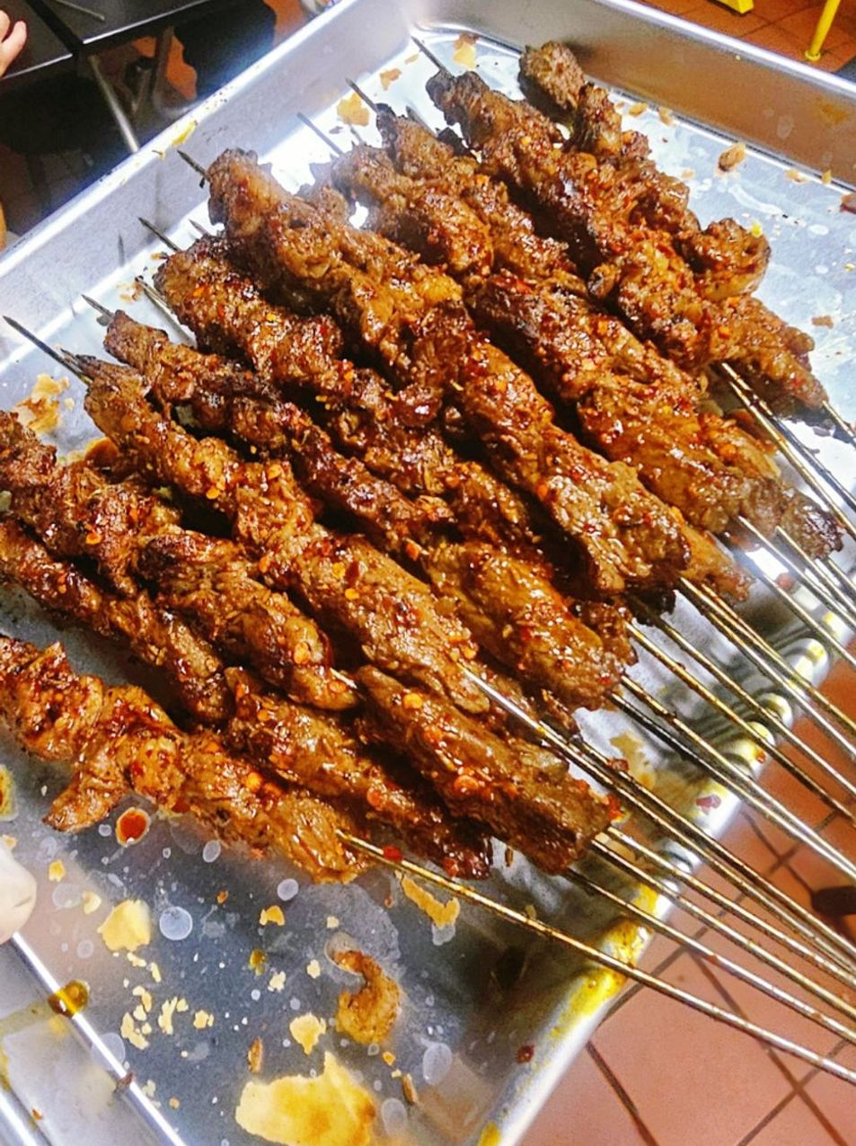 Many grilled meat skewers seasoned with chili on a metal tray