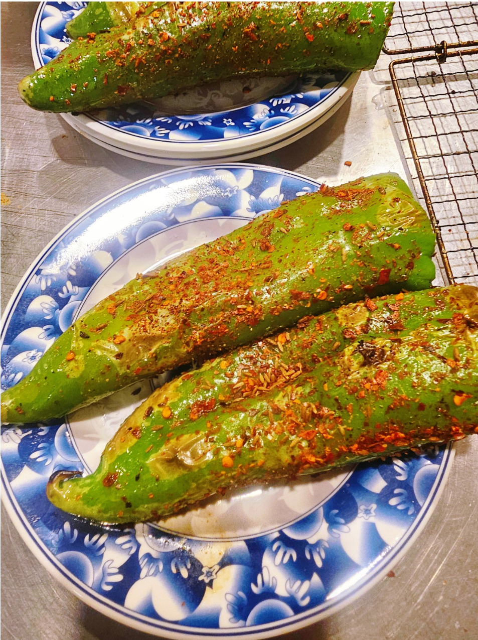 Roasted green peppers topped with chili flakes and cumin on a blue plate