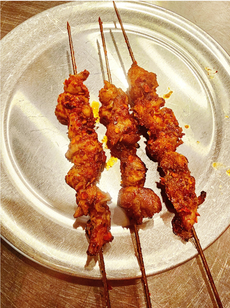 Three spicy grilled meat skewers on a metal plate