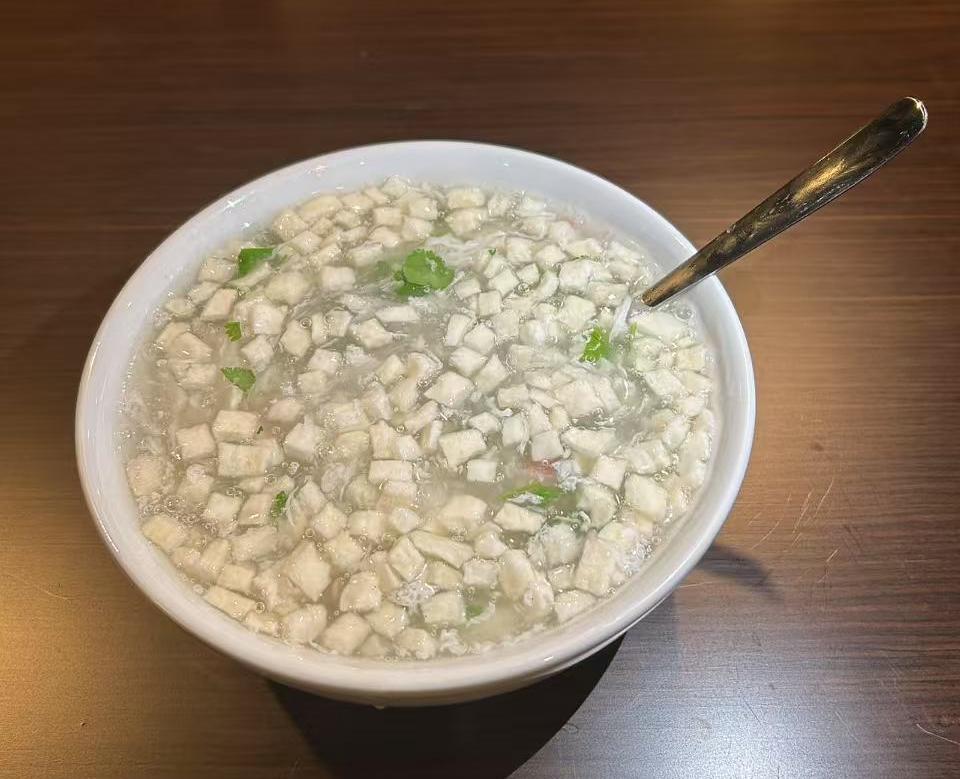 Silky minced tofu soup garnished with chopped green onions in a white bowl