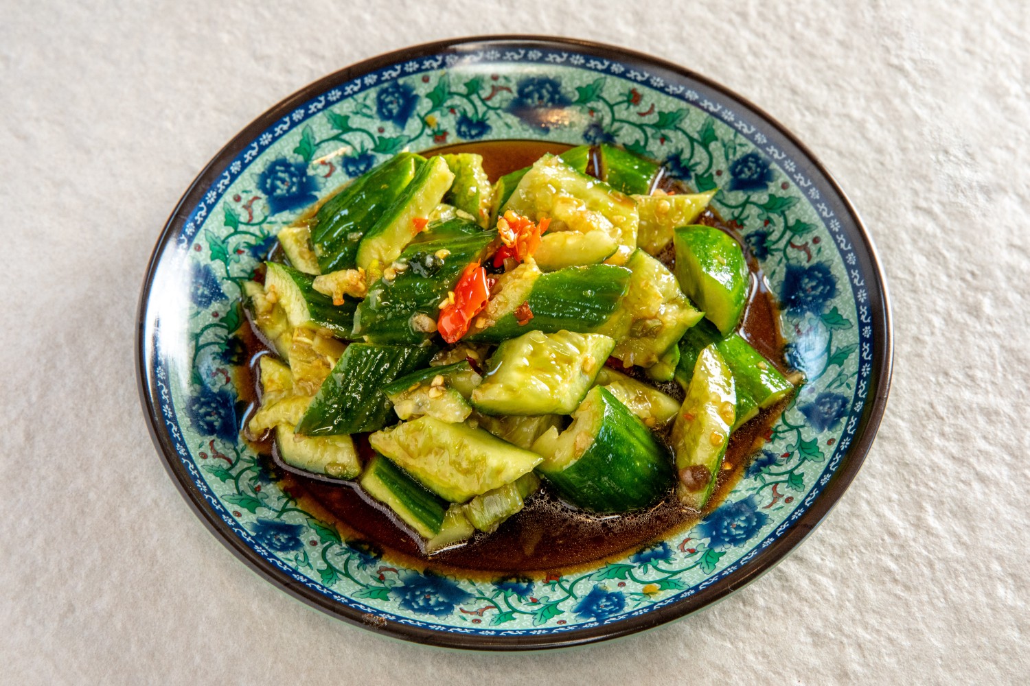 A plate of smashed cucumber salad with garlic, chili, and soy sauce dressing on a floral blue dish at Hunan Heat, a Chinese Restaurant in Long Island City