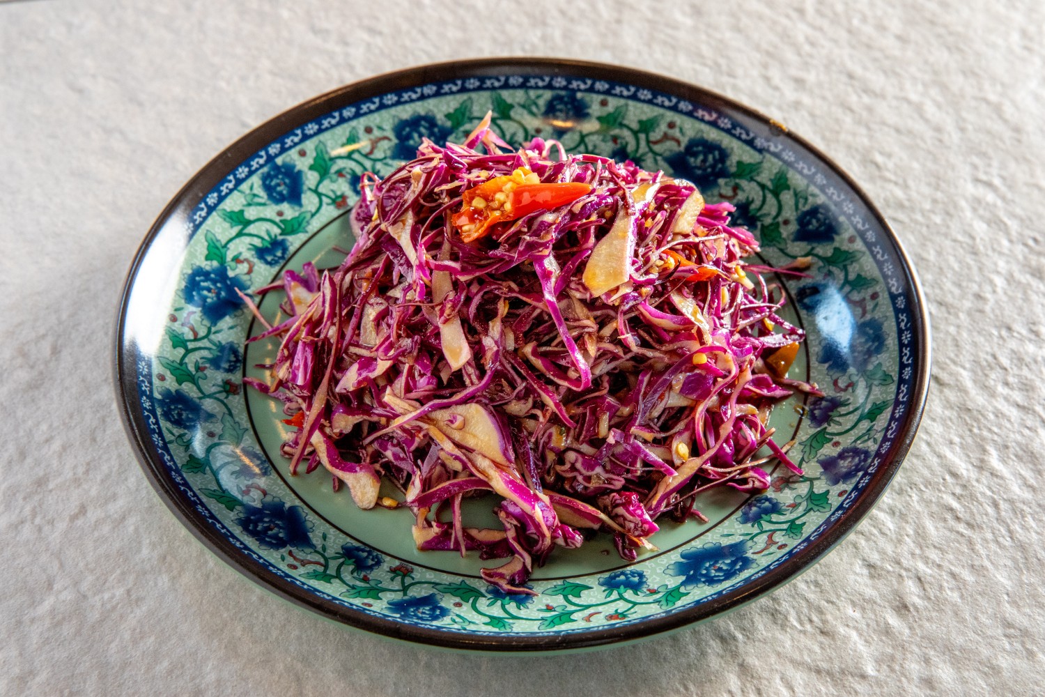 A plate of shredded purple cabbage slaw with chili and sesame seeds on a decorative dish at Hunan Heat, a Chinese Restaurant in Long Island City