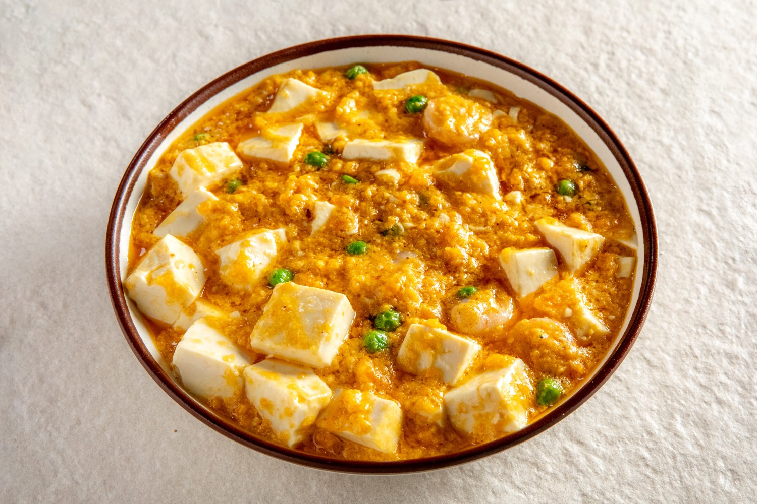A bowl of tofu cubes in golden crab roe sauce garnished with green peas at Hunan Heat, a Chinese Restaurant in Long Island City
