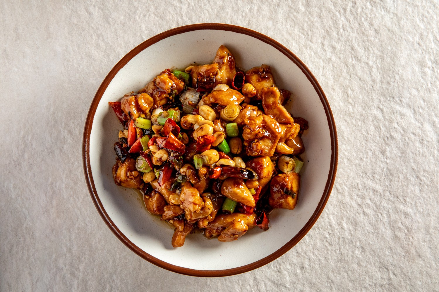 A bowl of kung pao chicken with peanuts, dried chilies, and scallions in savory sauce at Hunan Heat, a Chinese Restaurant in Long Island City