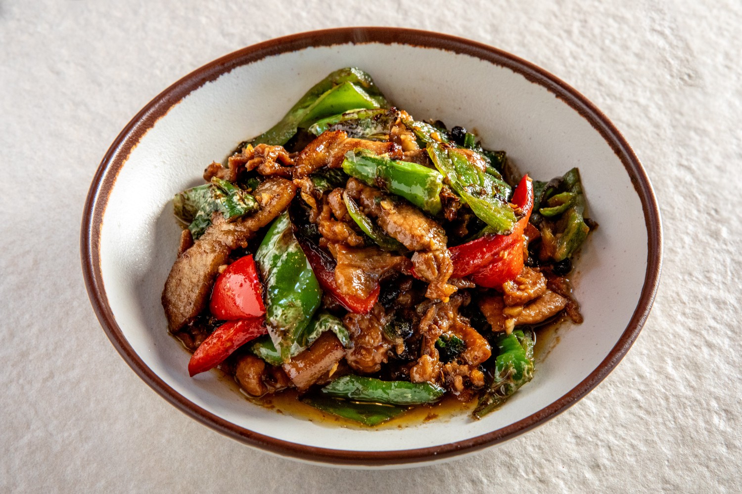 A bowl of Hunan-style stir-fried pork slices with green and red peppers in spicy sauce at Hunan Heat, a Chinese Restaurant in Long Island City