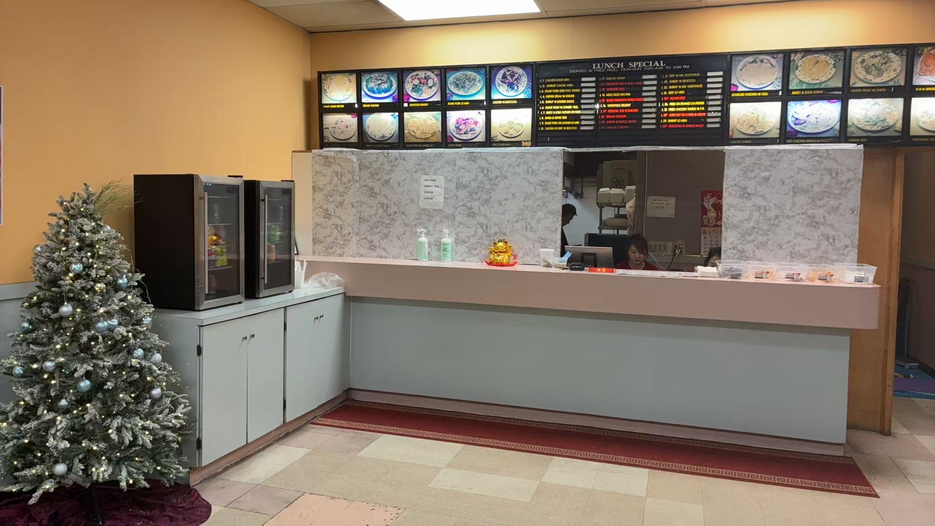Restaurant counter with staff, menu display above, and a decorated Christmas tree to the side.