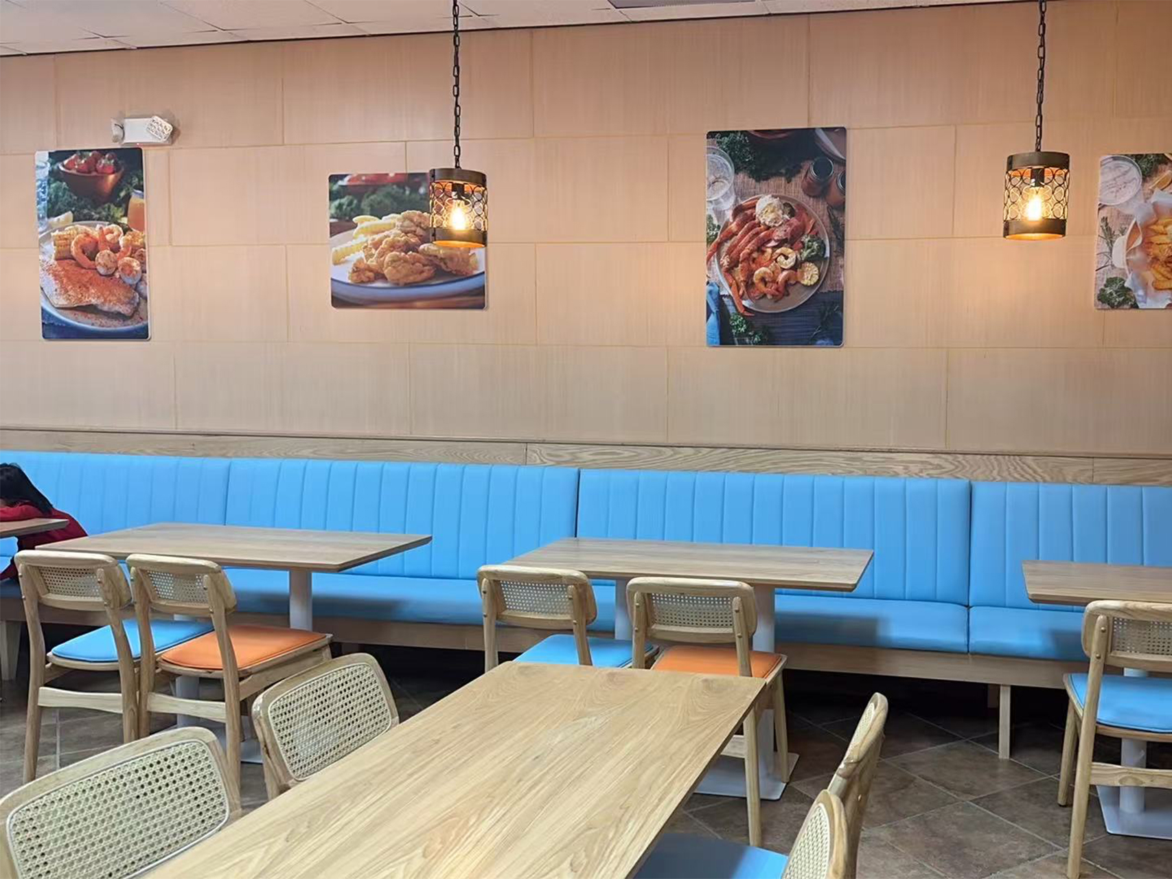 Dining area with blue booths, wooden tables, and food posters on the wall.