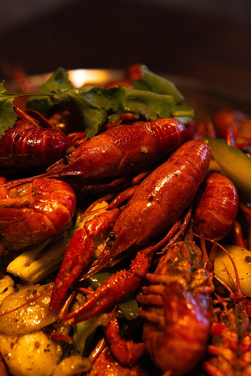 Close-up of glossy spicy crawfish with cilantro at 梦幻冰季 - ICERA，a Asian Fusion BBQ Restaurant in New York