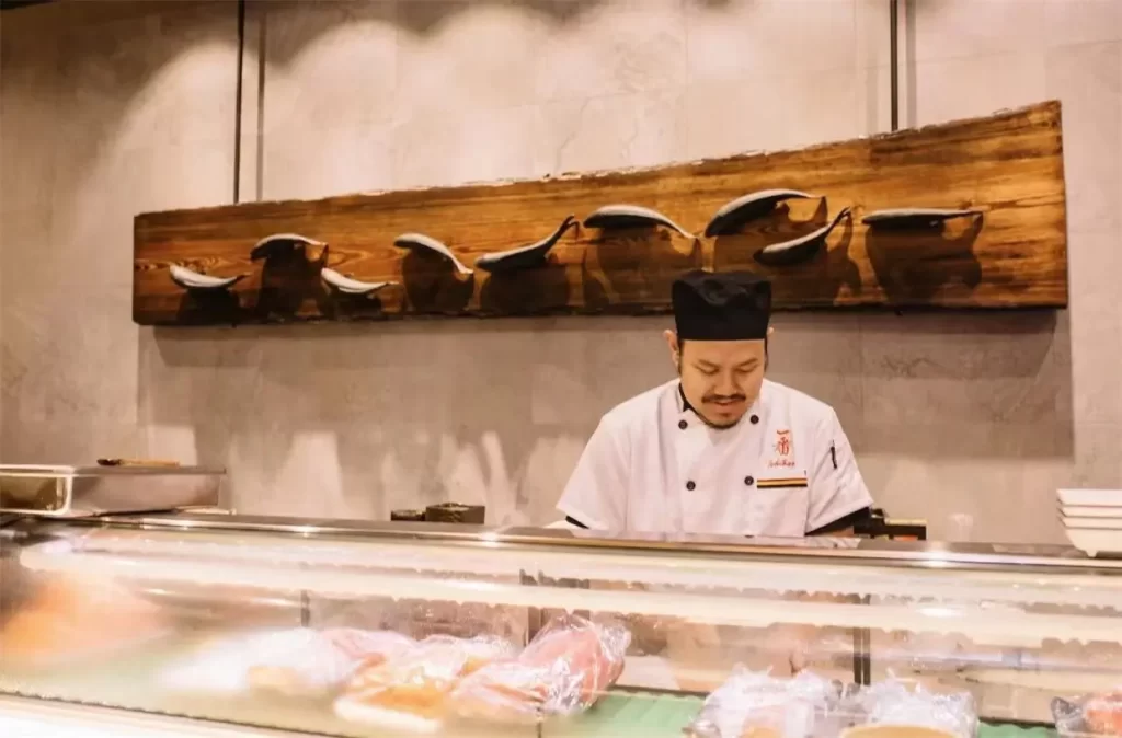 Skilled sushi chef preparing seafood behind glass display case at Ichiban Japanese Steakhouse & Sushi Bar, a Japanese Restaurant in Waco