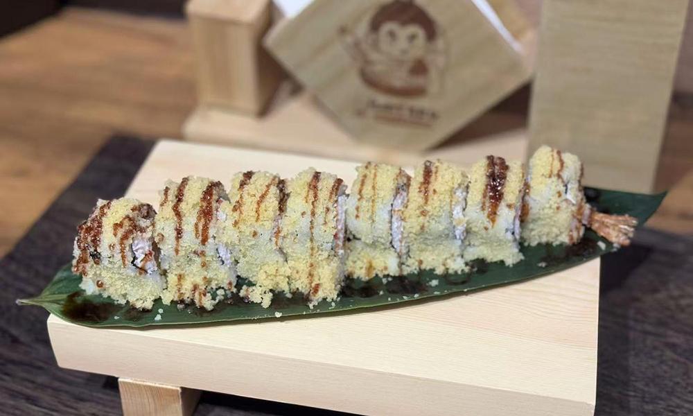 Crispy tempura sushi roll drizzled with brown sauce, served on green leaf atop wooden board at Ichitaru Ramen, a Ramen restaurant in Carlsbad