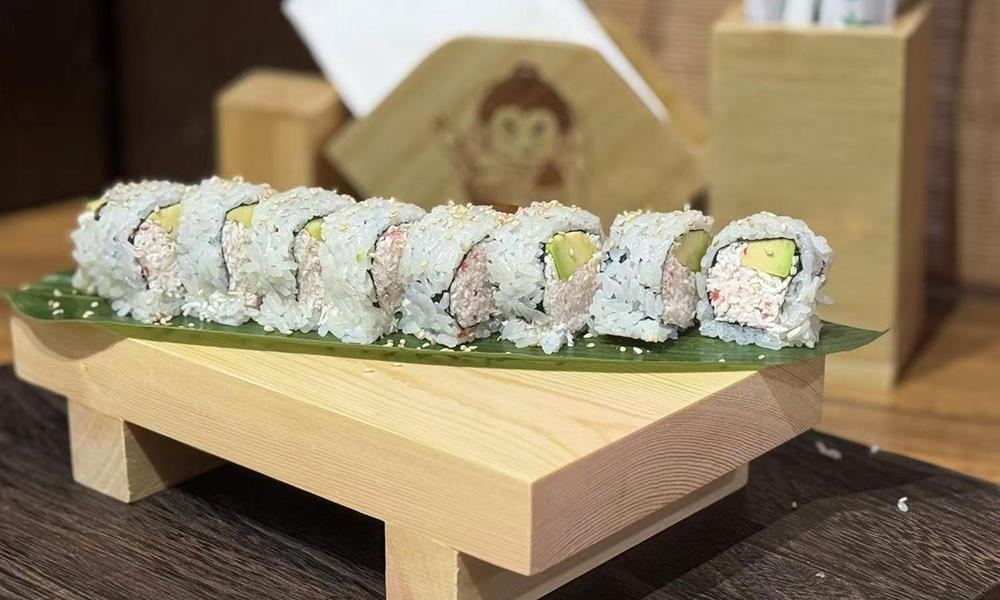 Sushi roll slices with avocado and crab filling arranged on leaf over wooden sushi stand at Ichitaru Ramen, a Ramen restaurant in Carlsbad