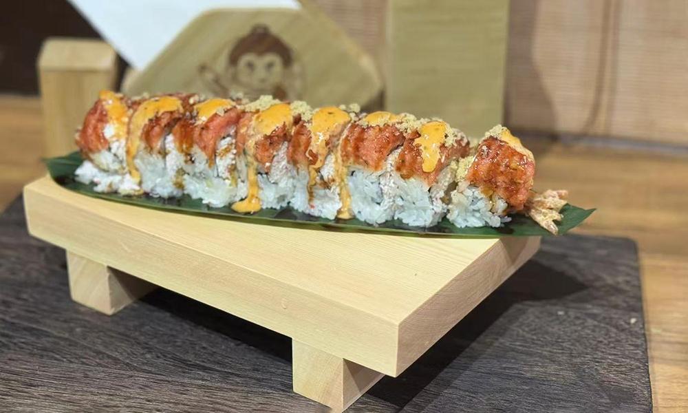 Spicy topped sushi roll with orange sauce, served on green leaf over wooden serving board at Ichitaru Ramen, a Ramen restaurant in Carlsbad