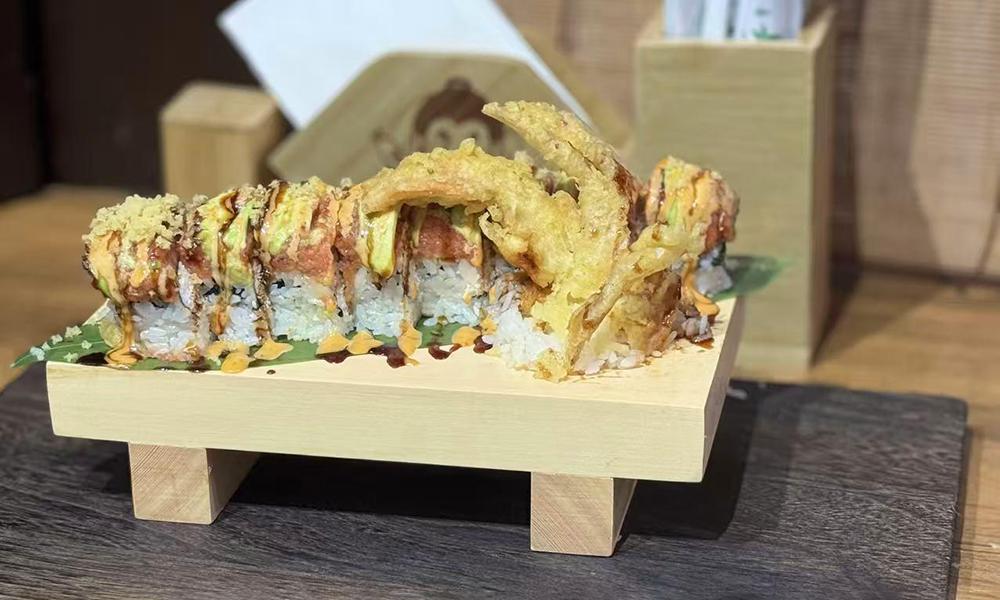 Tempura sushi roll garnished with fried seafood and brown sauce on wooden platter at Ichitaru Ramen, a Ramen restaurant in Carlsbad