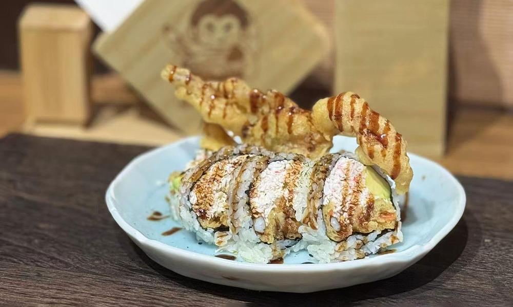 Sushi roll with tempura shrimp and sauce drizzle, served on light blue round ceramic plate at Ichitaru Ramen, a Ramen restaurant in Carlsbad
