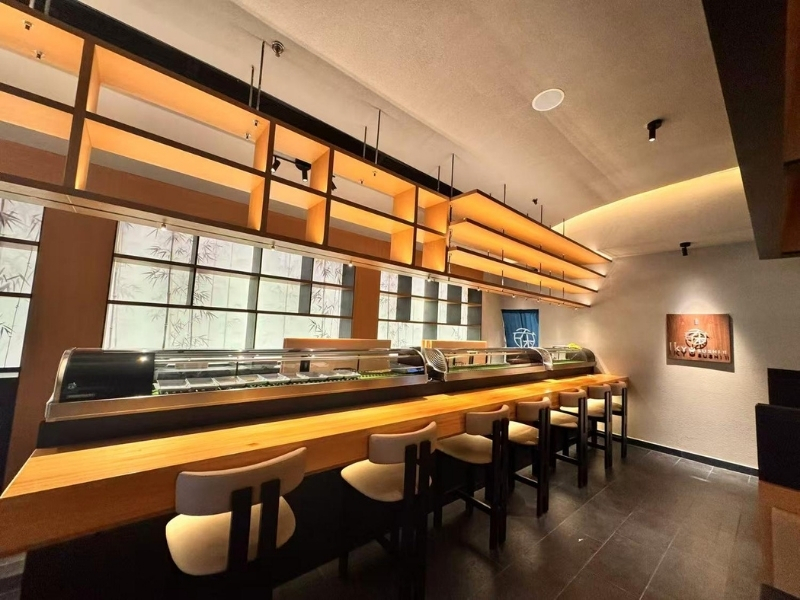 Ikyu-Sushi-II-Japanese-Restaurant-Sushi-Bar-New-York Sushi bar area in a Japanese restaurant, featuring a long wooden counter, bar stools, a Japanese Restaurant in New York.
