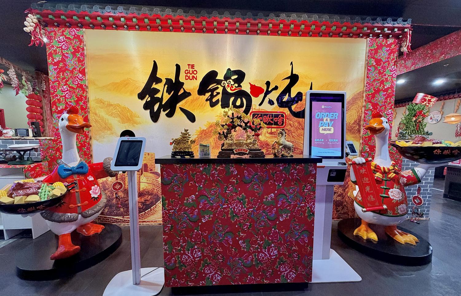 Red-themed hot pot shop with goose statues and order kiosk at Iron Pot Stew Kitchen, a Chinese Restaurant in Santa Clara