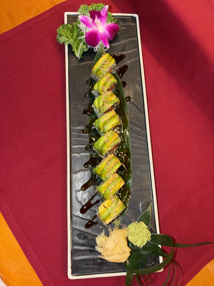 Avocado sushi roll drizzled with dark sauce and sprinkled with sesame seeds