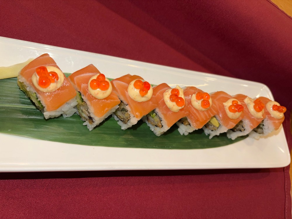 Salmon wrapped sushi roll topped with creamy sauce and salmon roe