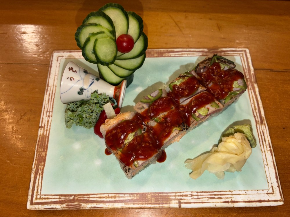 Seared fish roll topped with spicy red sauce, garnished with cucumber.