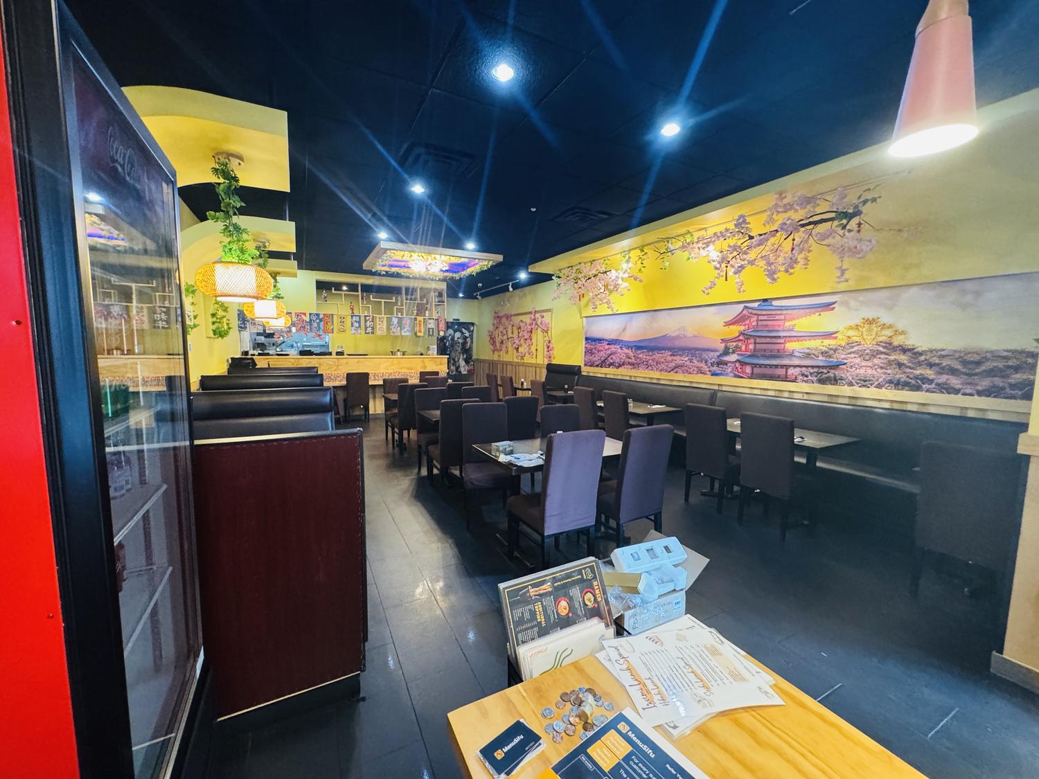 Interior of a Japanese restaurant with cherry blossom murals, dark booths, and a sushi bar under spotlights.
