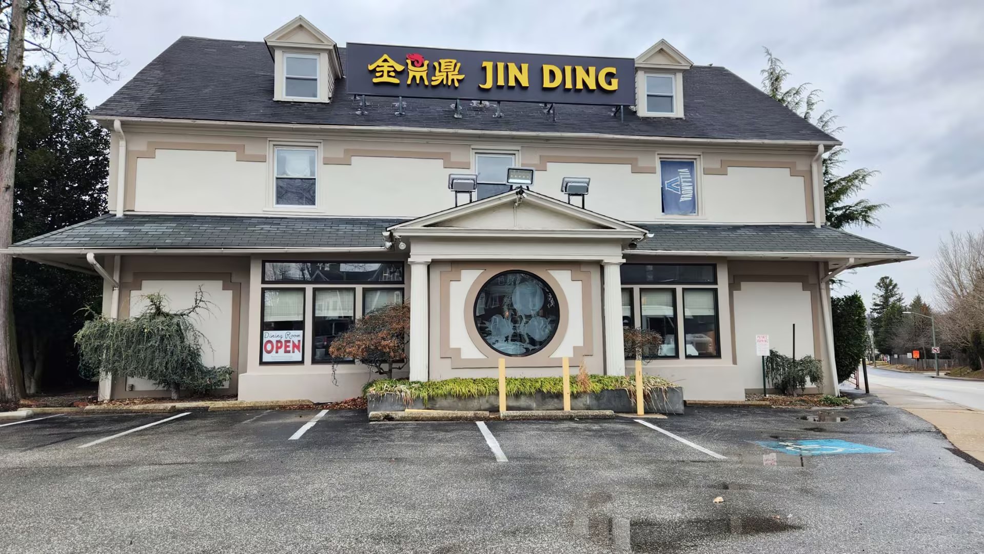Exterior of Jin Ding restaurant with black and yellow sign, circular window, open sign, and a wet parking lot.