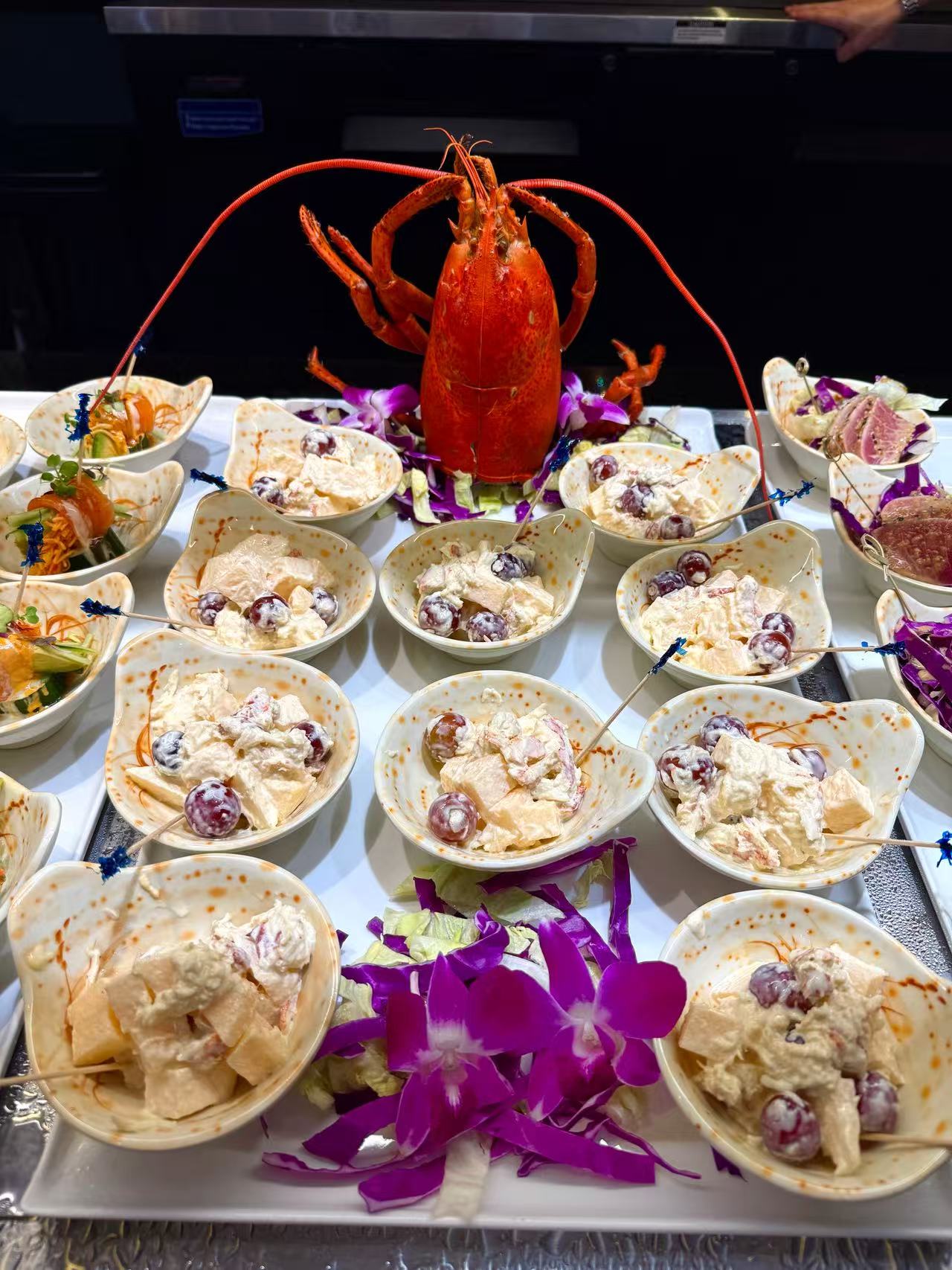 Lobster and Salad Appetizer - A lobster surrounded by small bowls of salad with grapes and other ingredients at JW Asian Seafood Buffet, a Buffet restaurant in Long Island City