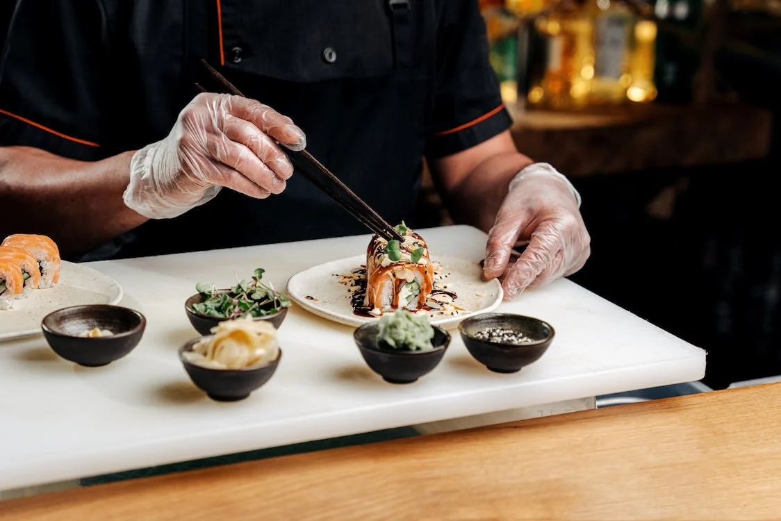 Chef plating a beautifully decorated sushi roll with fresh ingredients like microgreens  at Kakkoii Sushi, a Japanese restaurant in Malden