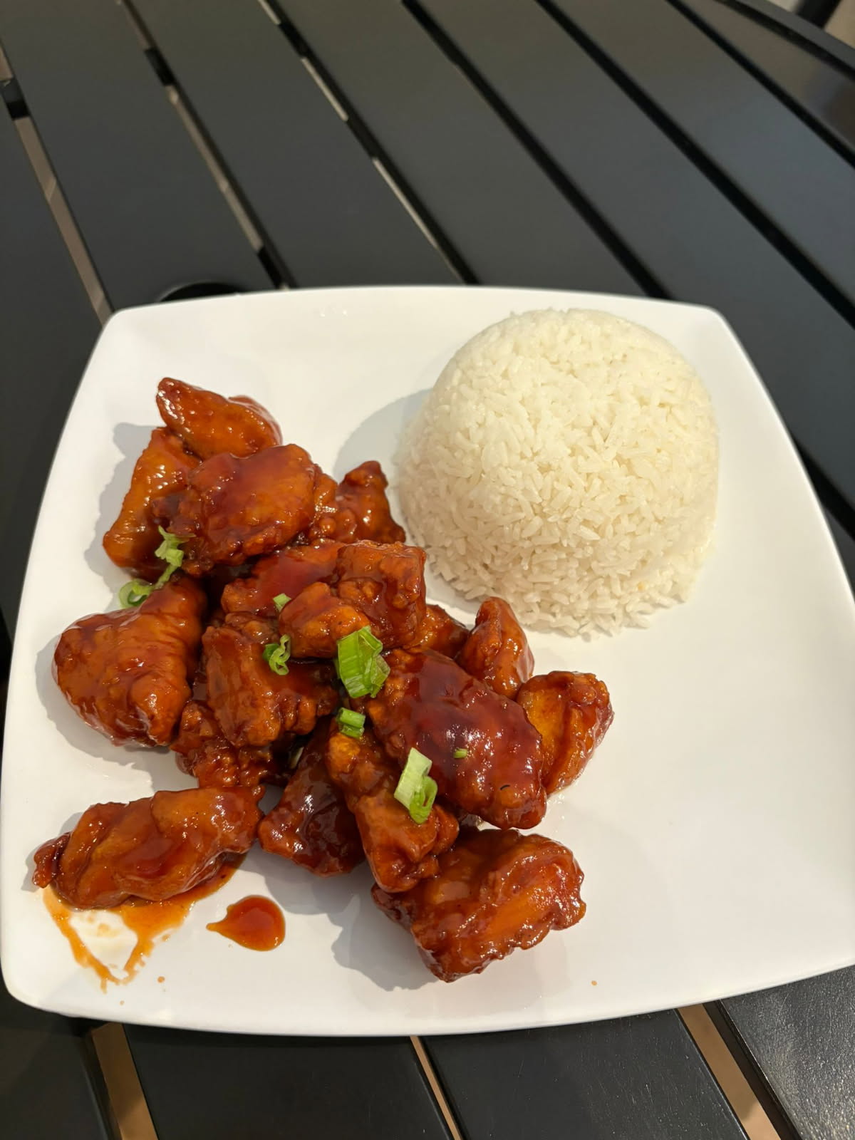 Sweet and Sour Chicken Rice includes white rice accompanied by pieces of chicken coated in a rich, red - hued sweet - and - sour sauce at Kao Mun Gai, a Thai restaurant in OK