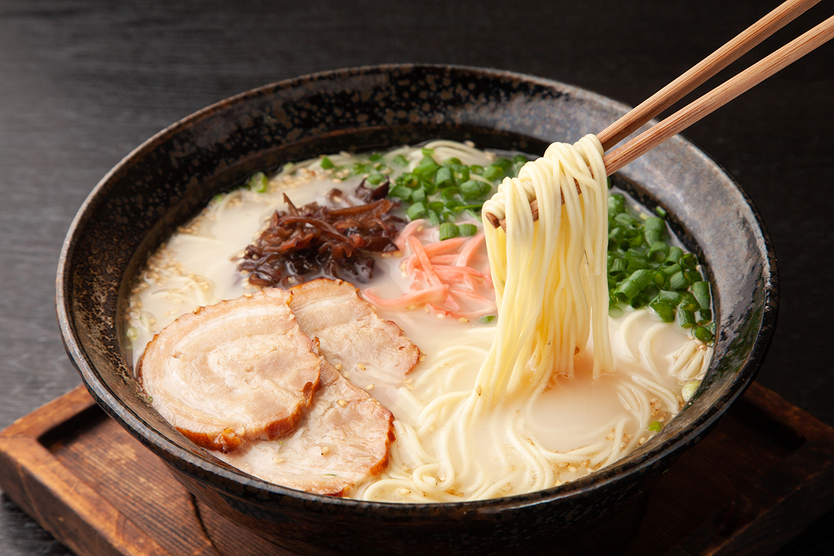 Tonkotsu ramen with sliced pork, green onions, and noodles lifted by chopsticks