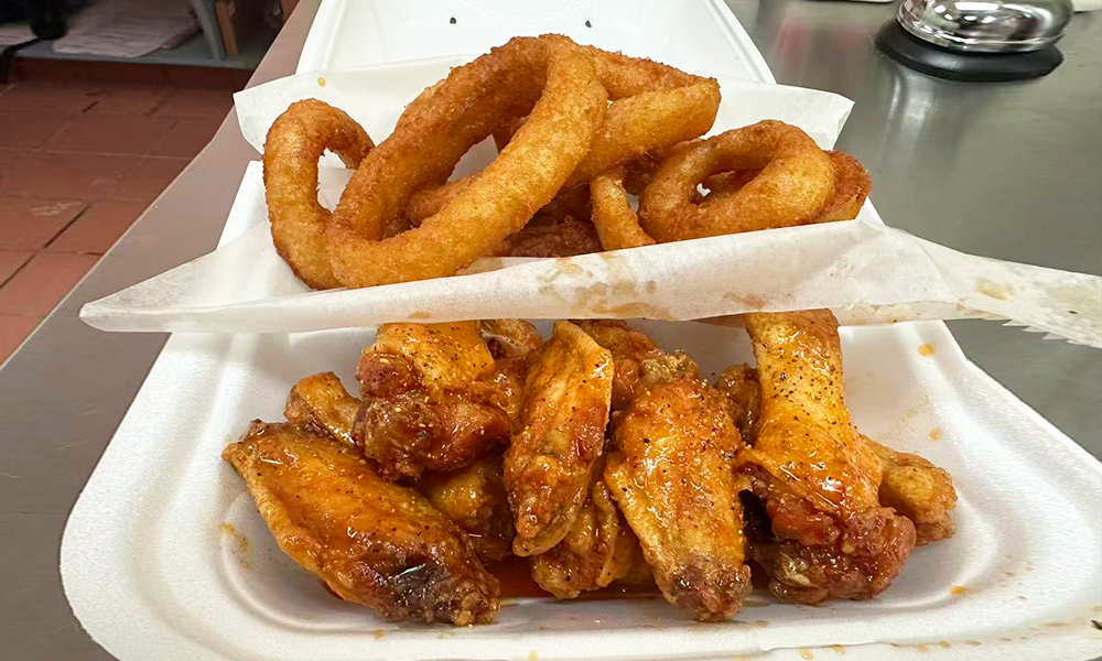 Buffalo sauce-coated chicken wings paired with crispy onion rings at Kick Off Wings, a Fast Food Restaurant in Carrollton