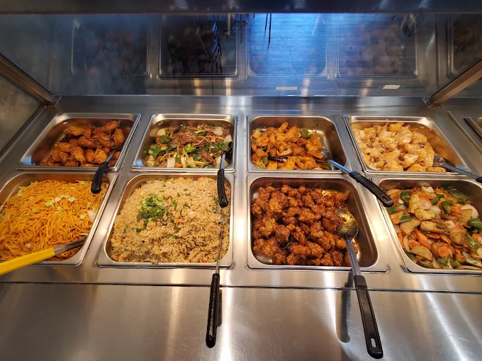 A buffet display of Chinese food with eight steaming hot dishes, including fried rice, noodles, and various stir-fries, served in metal trays.