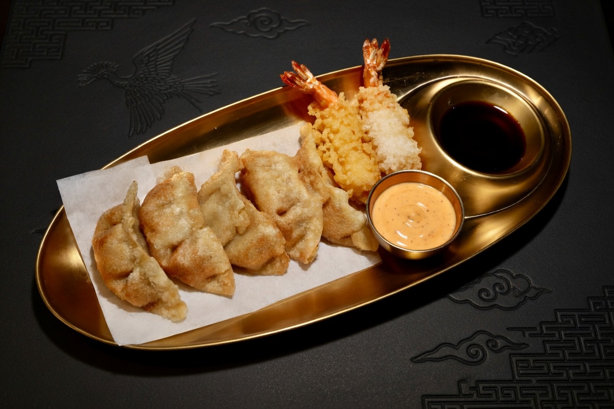 Golden platter with fried dumplings, shrimp tempura, and two dipping sauces on a dark surface.