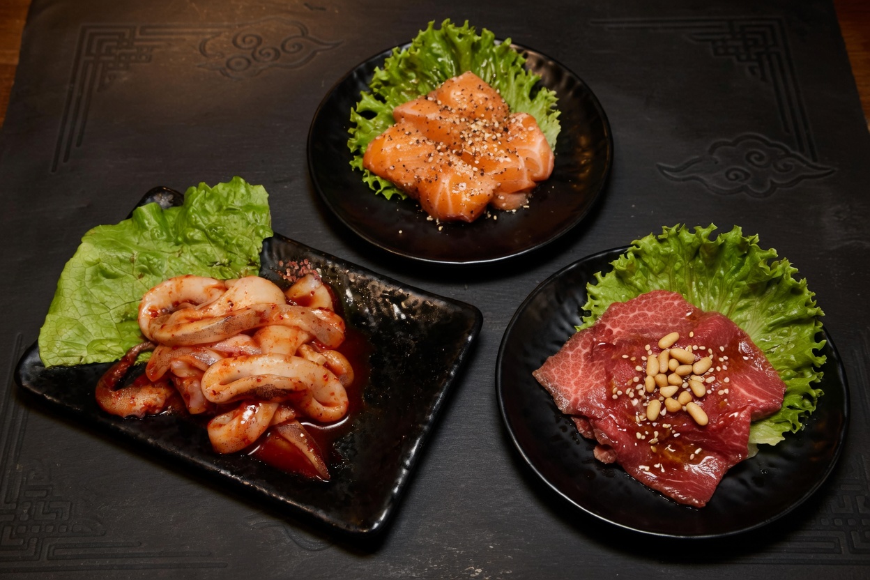 Three small plates of seasoned raw appetizers: spicy squid, cubed salmon, and sliced beef.