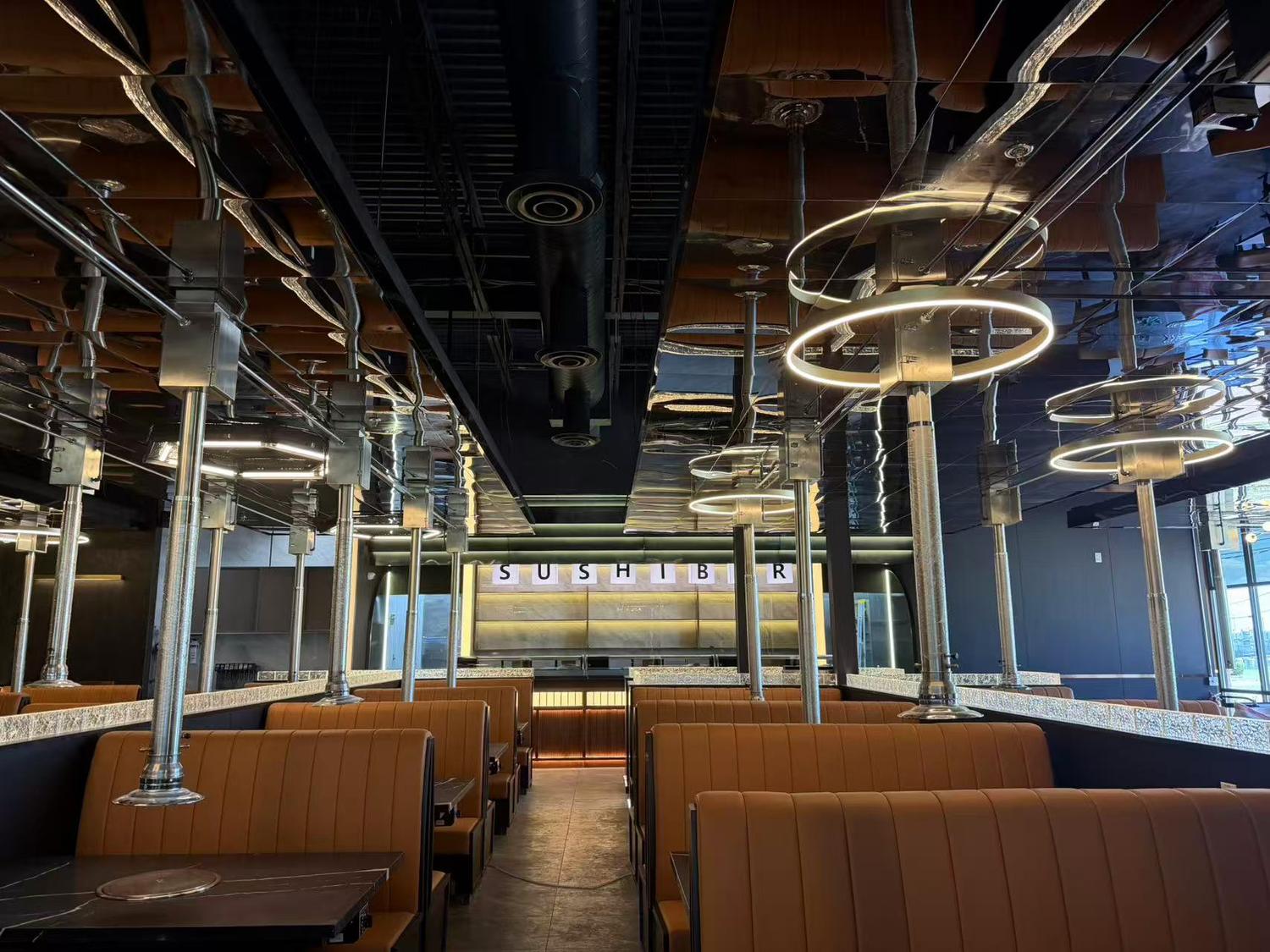 Modern interior of King House featuring tan booths, overhead BBQ exhaust vents, and a backlit sushi bar.