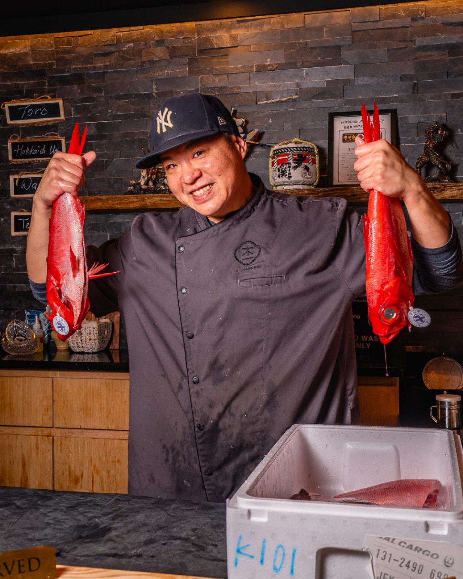 Chef holds two vibrant red whole fish for display at Ki Omakase, a Sushi Restaurant in Little Neck