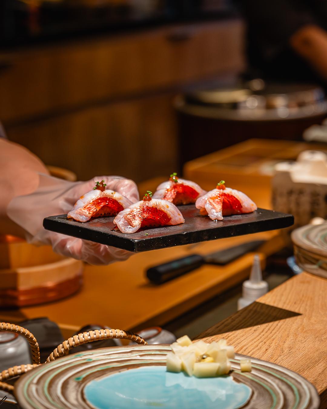 Gloved hand holds plate of fine fish nigiri at Ki Omakase, a Sushi Restaurant in Little Neck