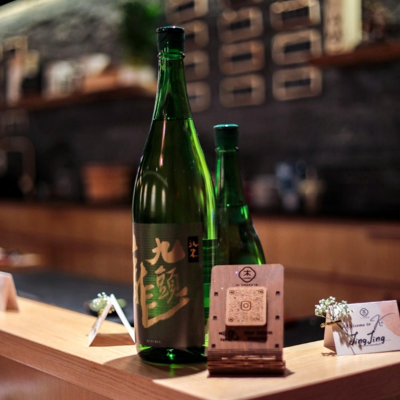 Green glass sake bottle next to guest name cards at Ki Omakase, a Sushi Restaurant in Little Neck