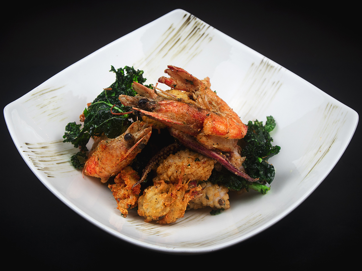 A white square ceramic bowl filled with crispy deep-fried head-on shrimp, battered calamari, and crunchy dark green kale leaves at KOI Restaurant, a Asian restaurant in Joplin