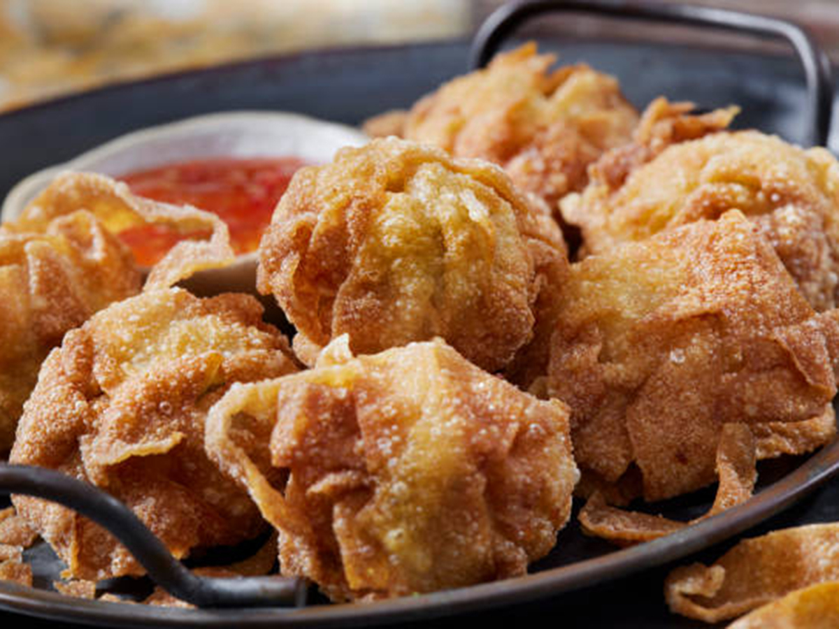 A dark metal tray filled with round, puffy deep-fried wontons featuring bubbly, crispy golden-brown wrappers, served with a small side bowl of red sweet chili sauce at KOI Restaurant, a Asian restaurant in Joplin