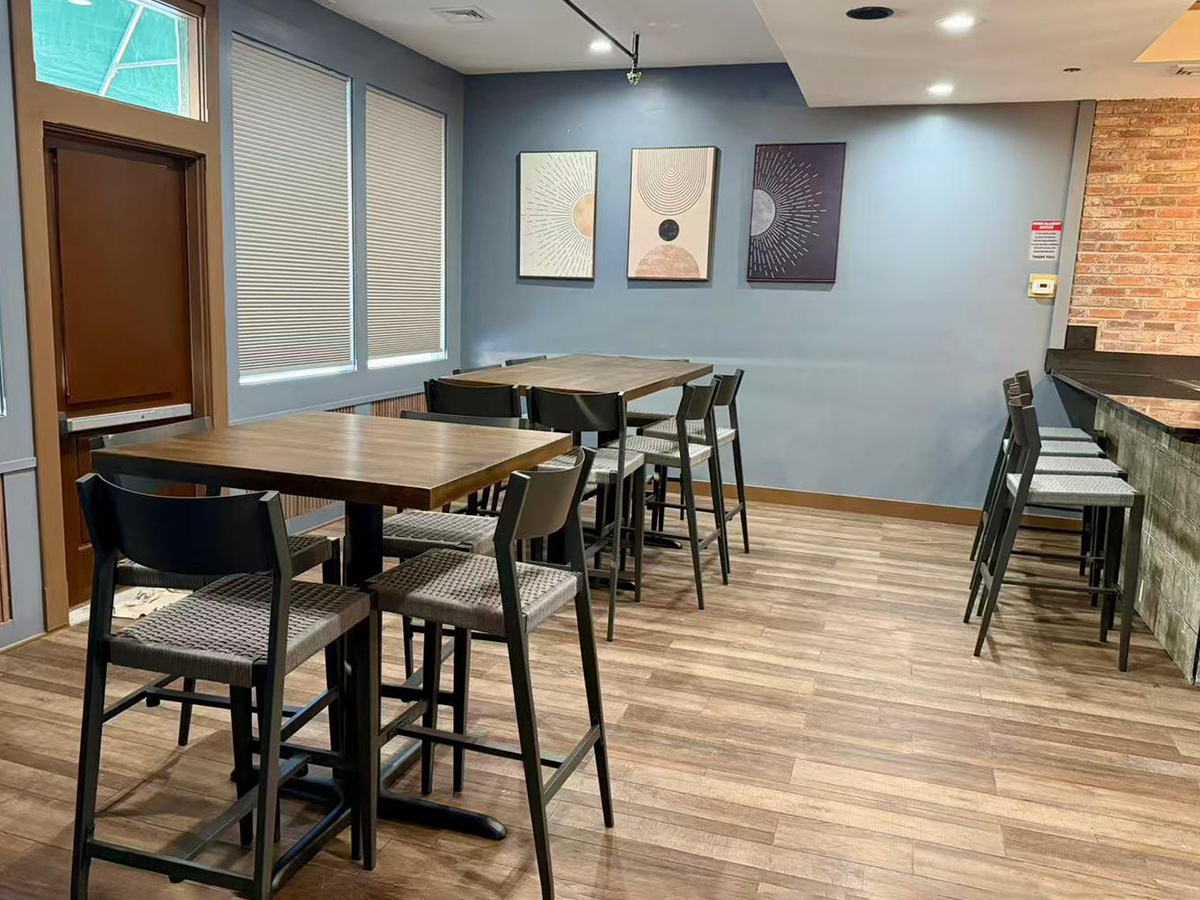 Dining area in Kojo Restaurant with tall wooden tables, black chairs, and wall art