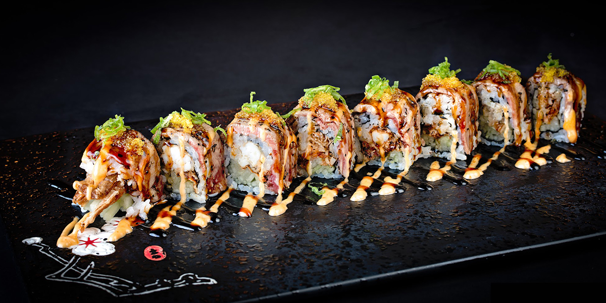 Seared beef layered gourmet sushi roll with dual savory sauces at Komeya Sushi & Ramen, a Japanese Restaurant in Spring