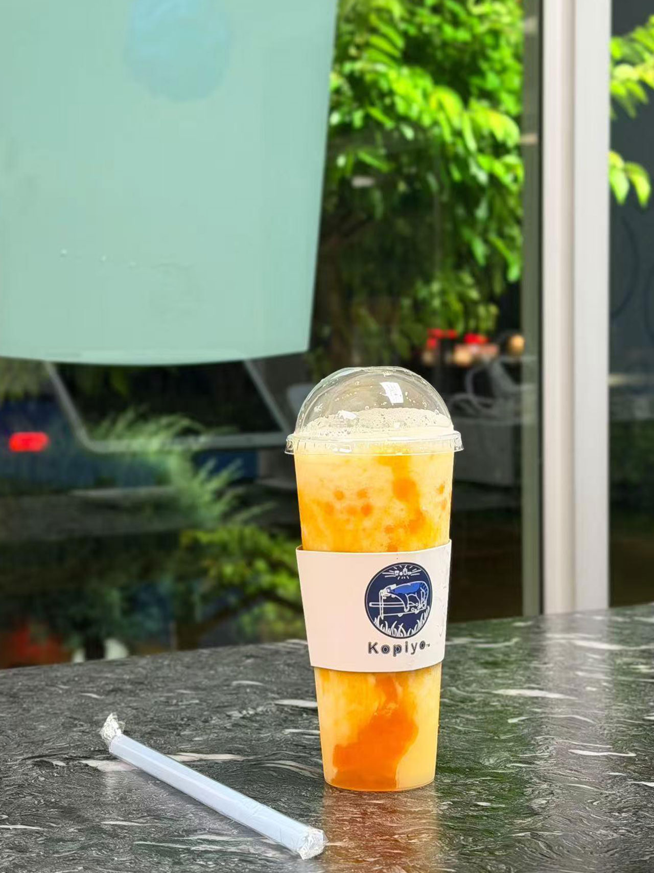 Orange mango iced beverage in a Kopiyo cup on a marble table at Kopiyo, a Coffee shop in Flowood