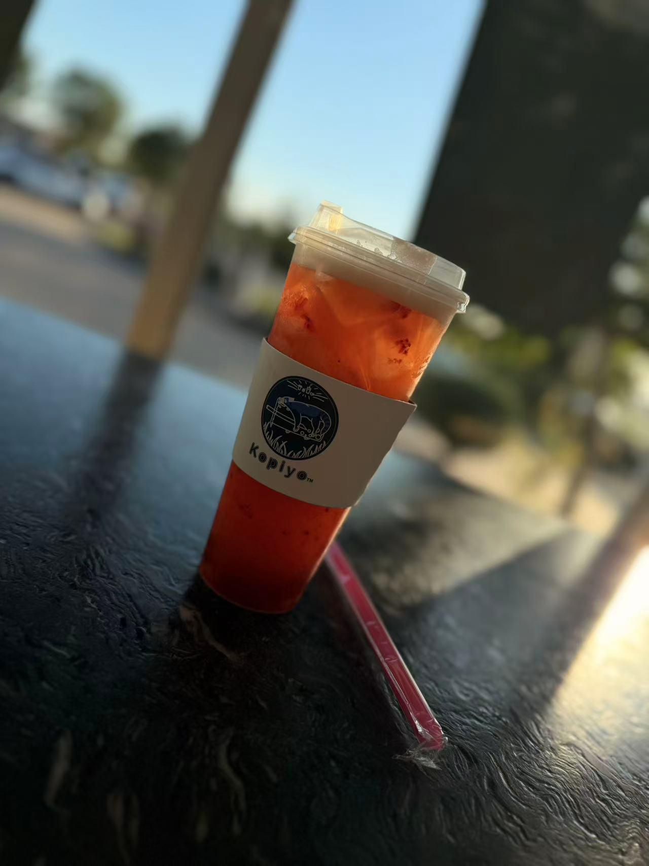 Red iced tea with fruit bits in a Kopiyo cup in sunlight at Kopiyo, a Coffee shop in Flowood