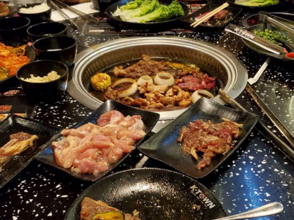 The dining table is filled with various ingredients and tableware, with a baking tray in the middle at K-Town Korean BBQ & Hotpot, a Korean BBQ & Hotpot Restaurant in Fort Wayne