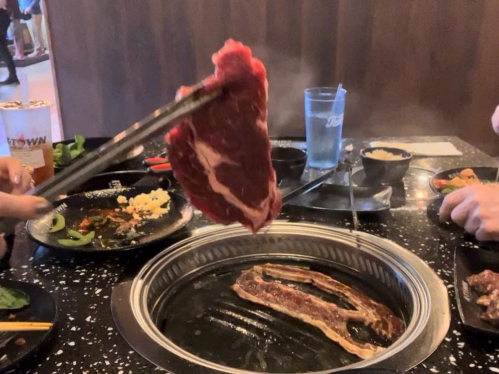 someone is grilling ingredients. There is meat on the baking tray at K-Town Korean BBQ & Hotpot, a Korean BBQ & Hotpot Restaurant in Fort Wayne