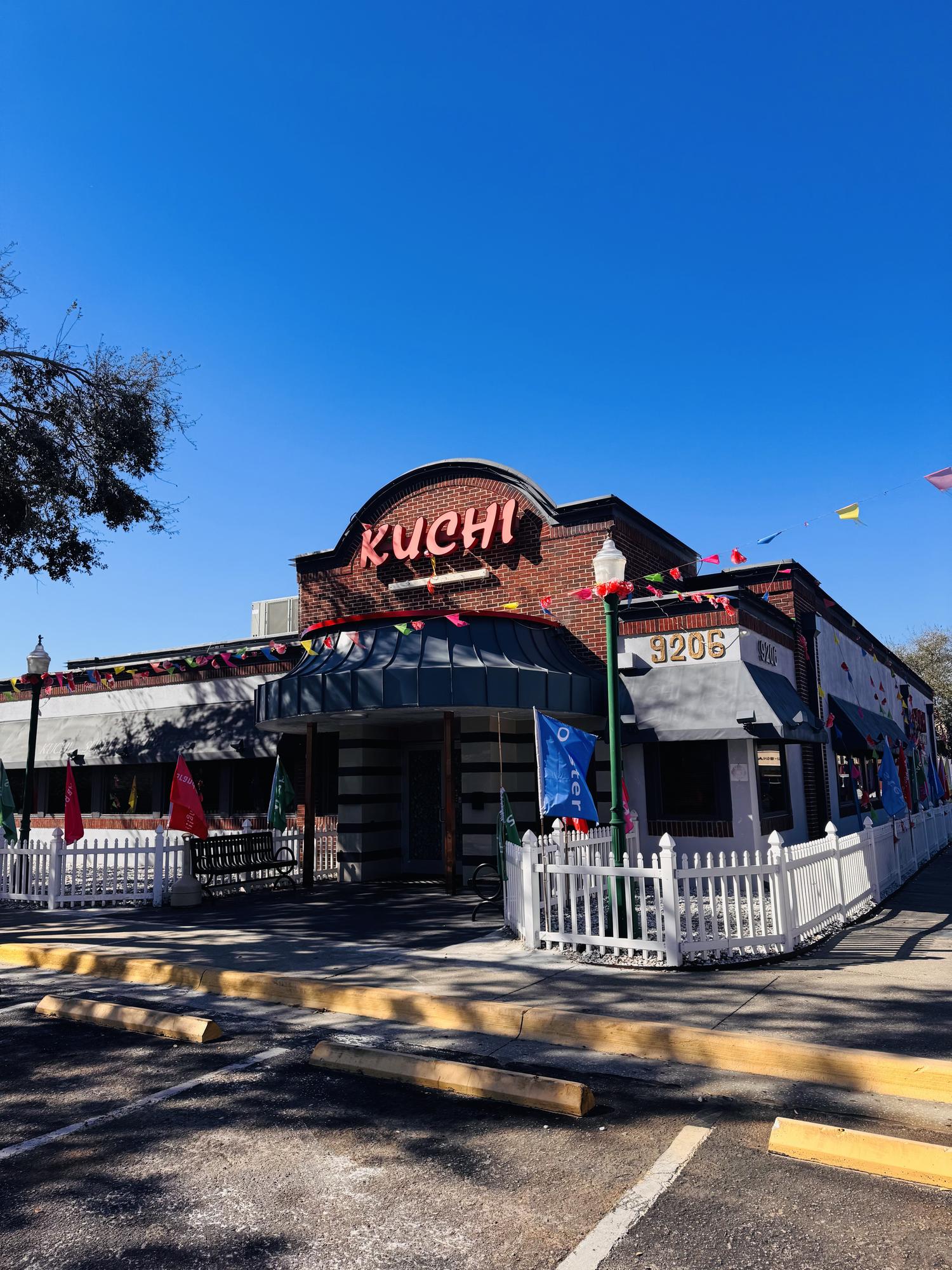 Charming brick exterior with festive flags and white picket fence at Kuchi, a Buffet Restaurant in Tampa