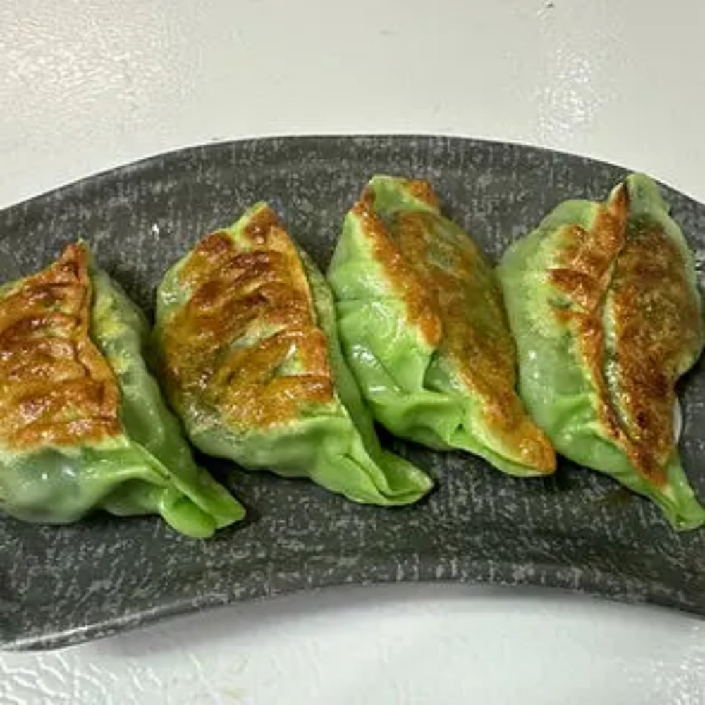 Four green pan-fried dumplings on dark plate
